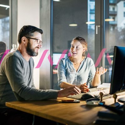 Image of a woman and man sitting in front of a desktop computer and engaging in conversation.