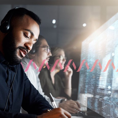 Photo of a row of contact center agents, shot from the side, as they handle calls from customers, take notes,  and look at their computer monitors. A series of small pink waves runs across the frame.