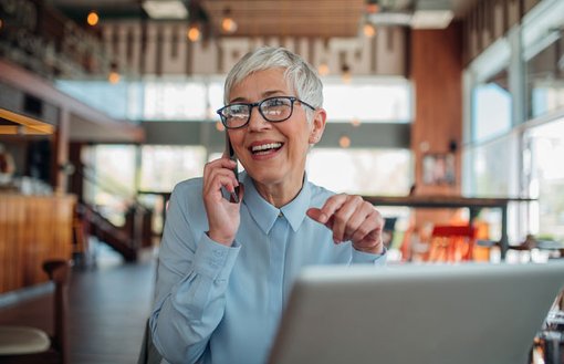 Image of woman on mobile phone sitting in a cafe in front of her laptop