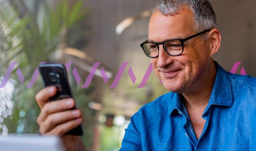 Photo of a smiling, casually dressed man reading something on his cellphone. In the background, a series of small purple wave forms run across the frame, representing communications.