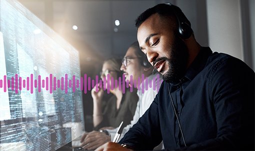 Photo of a row of tightly grouped contact center agents, seen from the side. The agents are looking at information on their computer monitors while engaging in phone conversations with customers. 