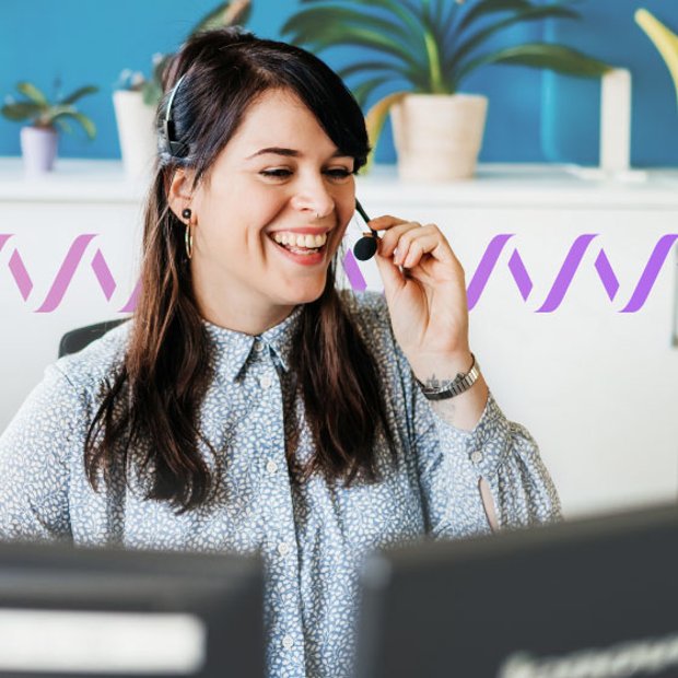 Photo of smiling agent talking to a customer through her headset. In the background, a series of small purple waves run across the frame, representing communications