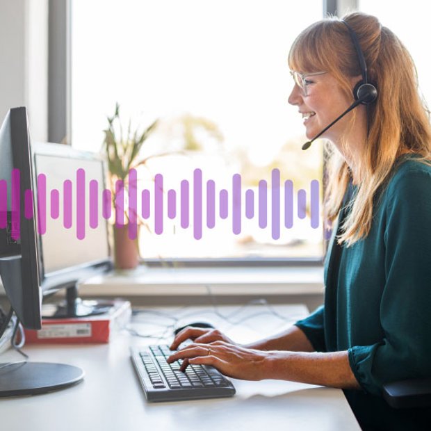 Photo of a smiling female call center agent sitting at her computer and talking to a customer through her headset. In the backgound, a small series of purple vertical lines run across the frame, representing communication.