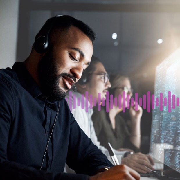 Photo of a row of call center agents dealing with customers on their phones while looking at data on the computer monitors. In the background, a series of small purple vertical lines runs across the frame.