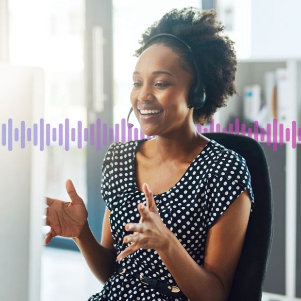 Photo of a smiling agent in an office gesturing with her hands as she talks to a customer on her phone headset. In the background, a series of small purple vertical lines runs across the frame.