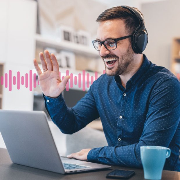 Photo of a smiling employee in an office sitting in front of his laptop. He is talking on his headset and gesturing. In the background, a series of small pink vertical lines runs across the frame.